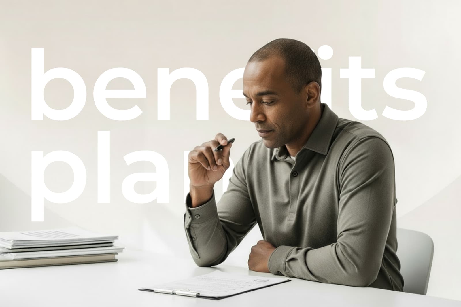 Man in a gray shirt sits at a desk, holding a pen and reviewing documents. Large text in the background reads "benefits plan."