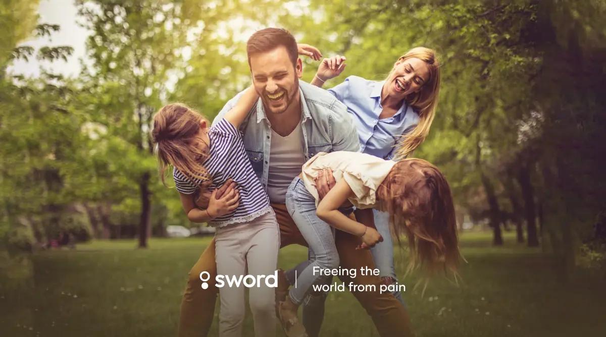 A joyful family of four playfully laughing in a park, with the text "sword: Freeing the world from pain" overlaid.
