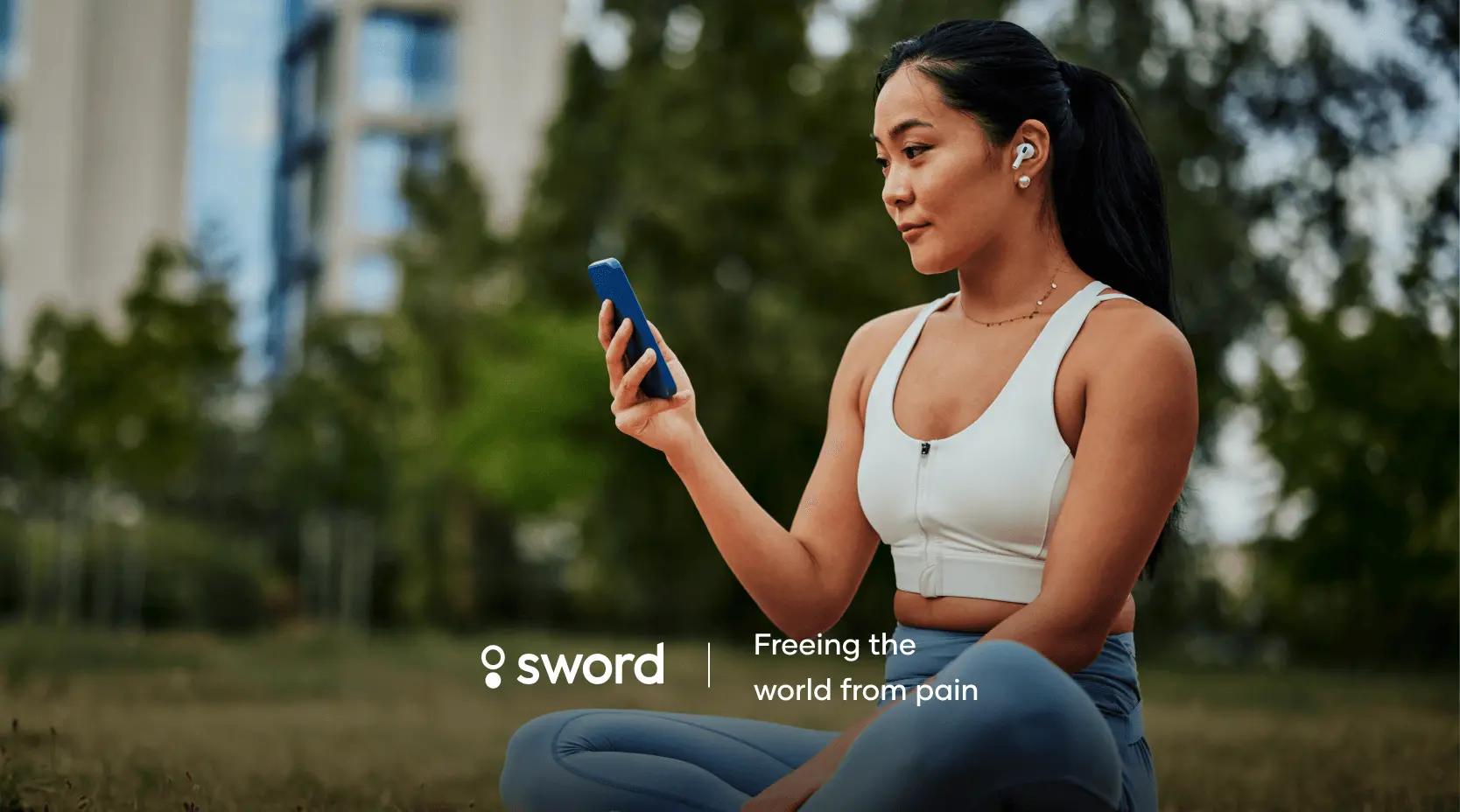 A woman in athletic wear sits outdoors, looking at her phone, with earbuds in. Text: "Sword - Freeing the world from pain."