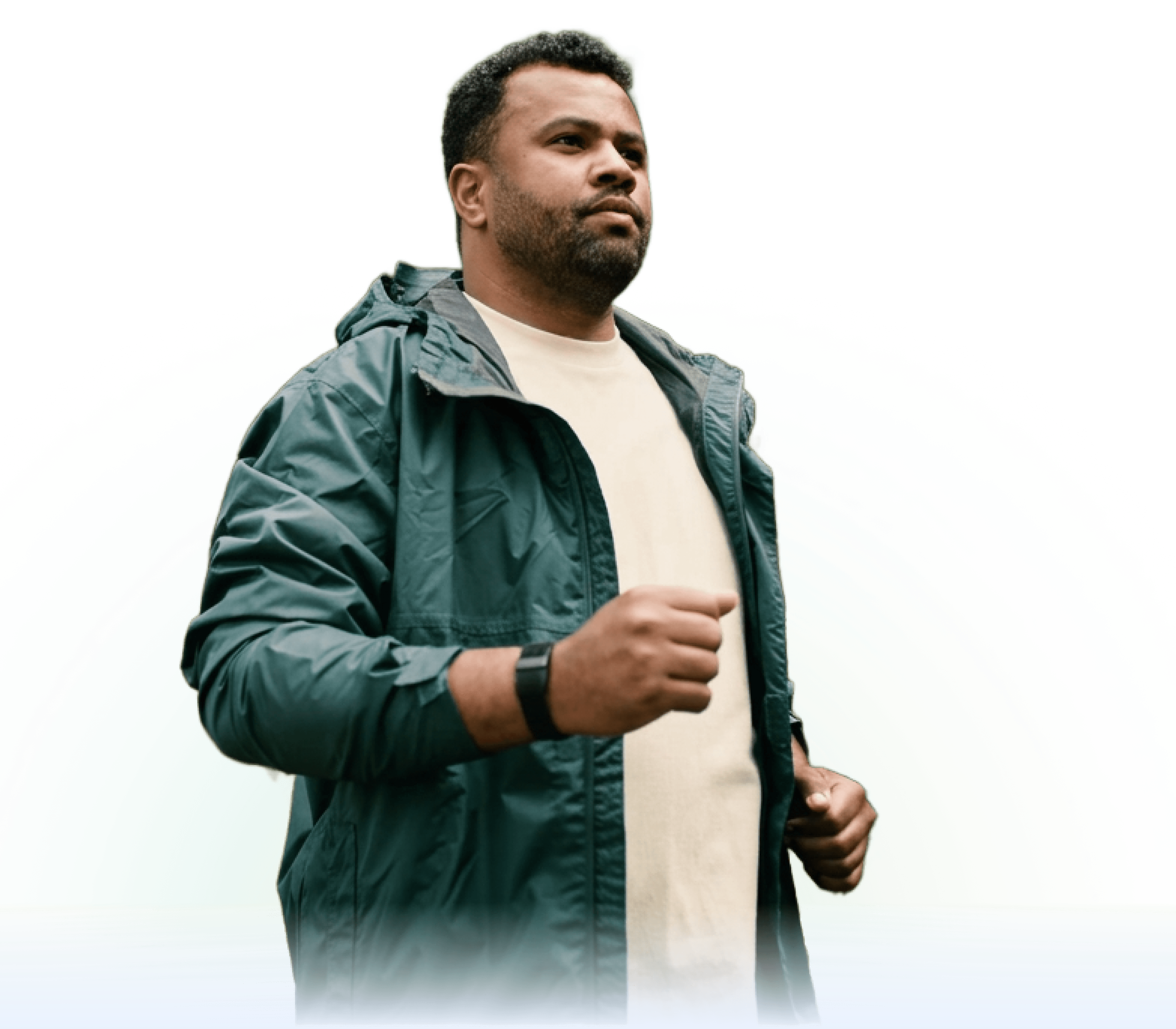 A man wearing a green jacket and beige shirt walks purposefully outdoors, looking ahead with a focused expression. He is wearing a smart watch on his left wrist.