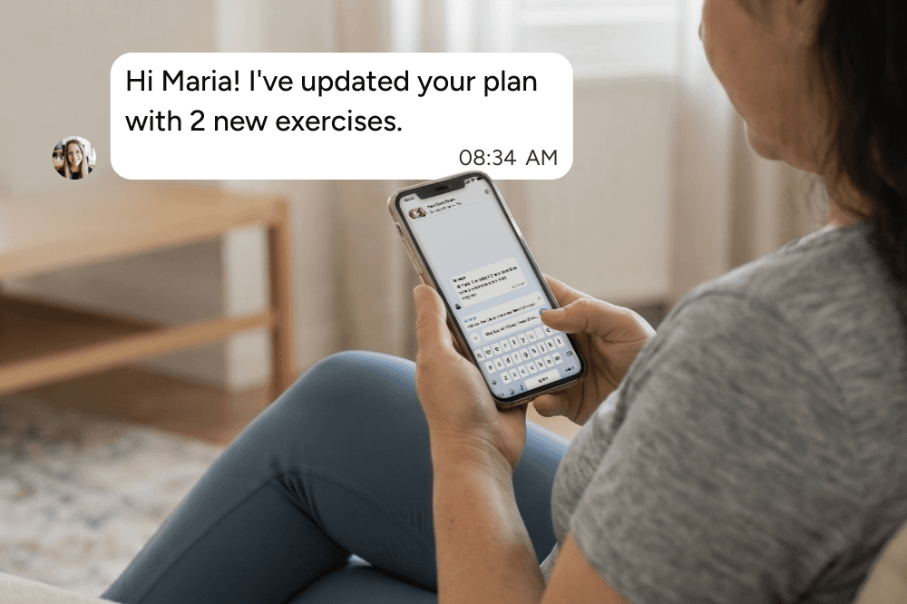 A woman sitting on a couch looks at her phone, reading a message that says, Hi Maria! Ive updated your plan with 2 new exercises. The time on the message is 08:34 AM.