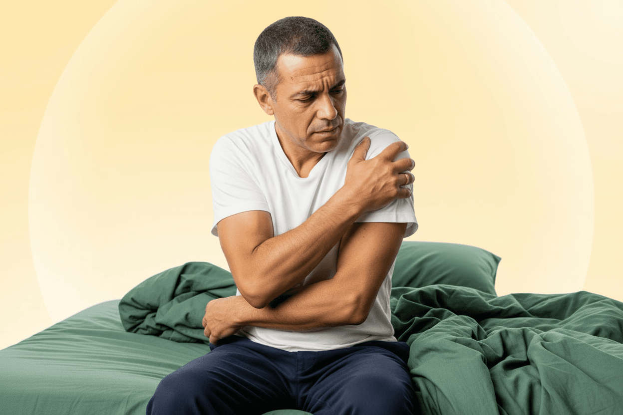Man sitting on a bed holding his shoulder, showing discomfort linked to shoulder pain after sleep.