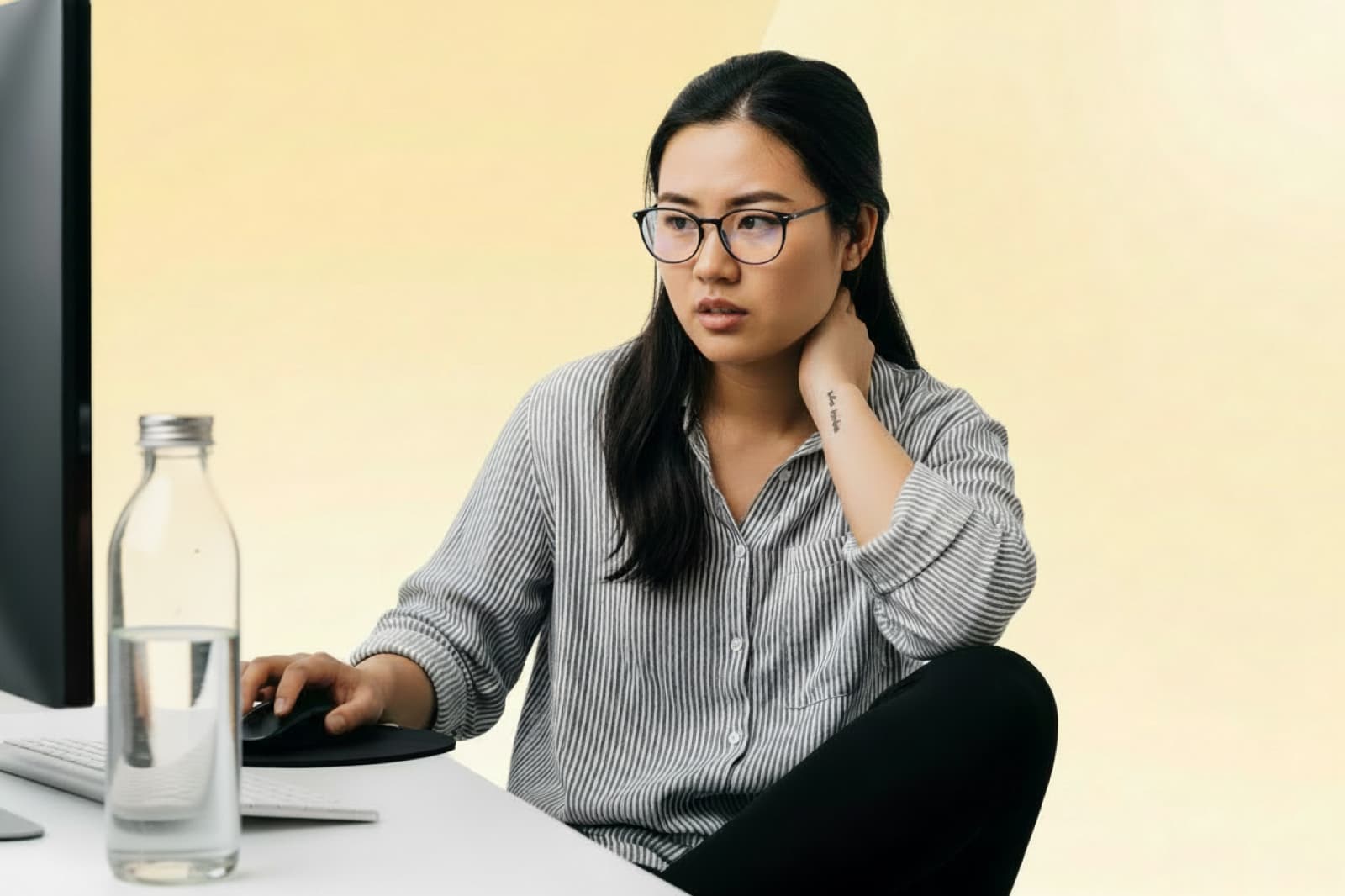 Woman working on a laptop at a desk, touching her neck as she experiences strain from desk work.