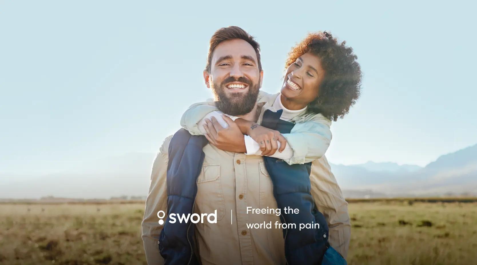 A smiling man carries a joyful woman on his back in an open field. The text reads, "Sword: Freeing the world from pain."