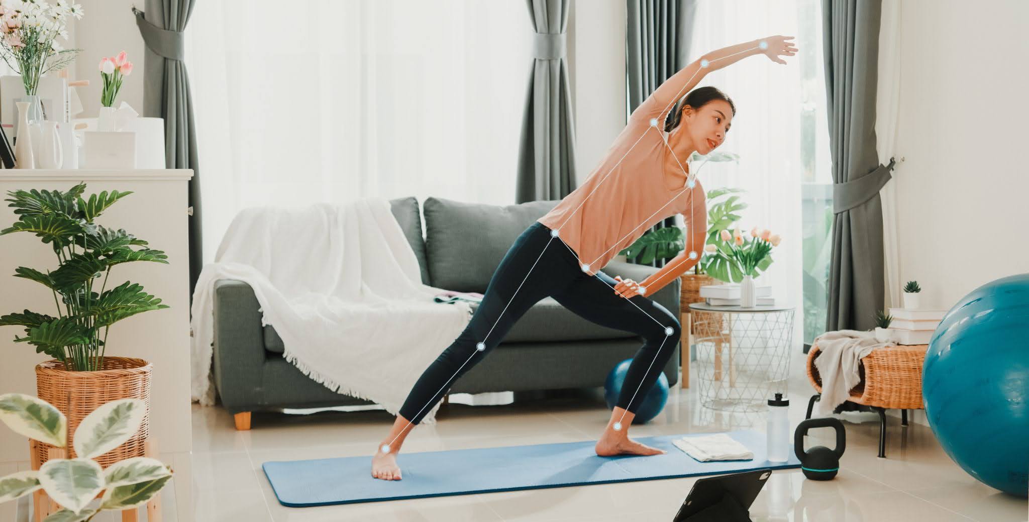 Woman practicing yoga on a mat in a living room, surrounded by plants, a sofa, and exercise equipment.