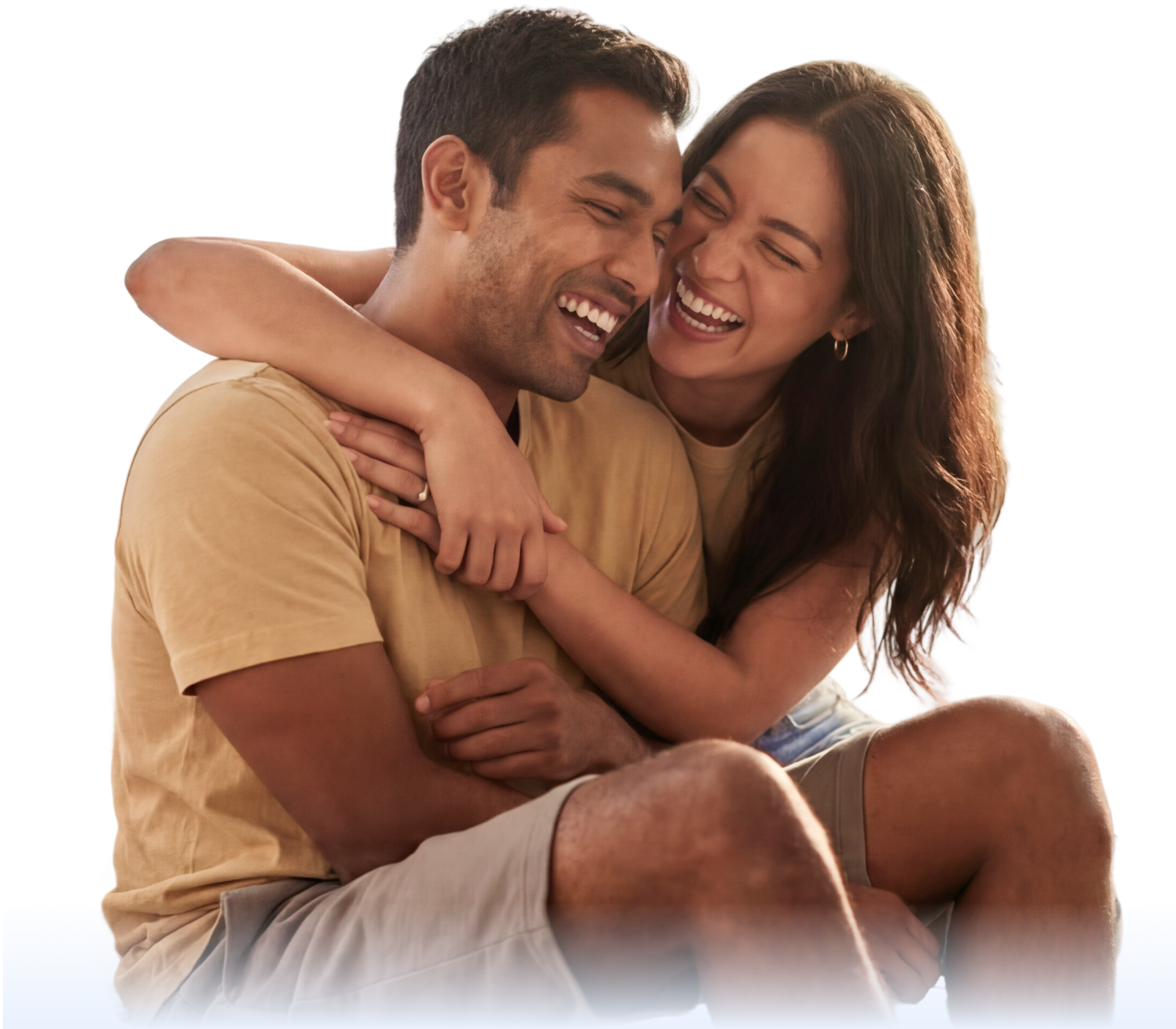 A couple sits close together, smiling and laughing. The woman has her arm around the man, and they appear happy and relaxed, wearing casual clothes on a white background.