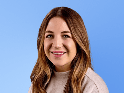 Woman with long brown hair, smiling, wearing a light sweater, against a blue background.
