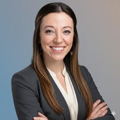 Picture of Jennesa smiling, with long hair in a gray blazer and white blouse, standing with arms crossed against a gradient background.