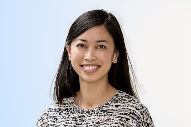 A woman with straight, dark hair and a patterned top smiles at the camera against a light blue and white background.