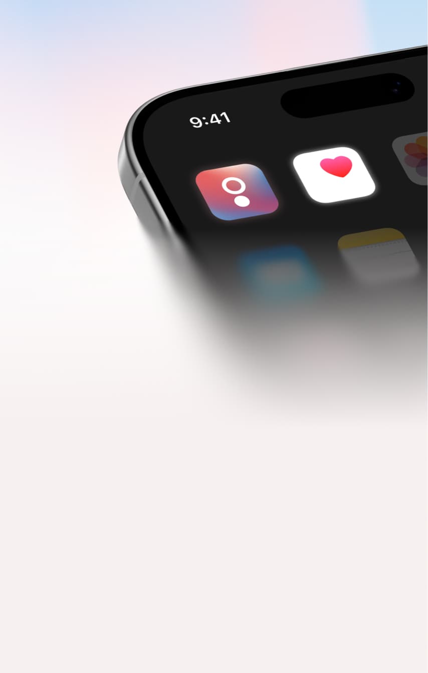 Close-up of a smartphone screen showing app icons, including a red heart on a white square and a circular icon. The time displayed is 9:41. The background is softly blurred in light pastel colors.